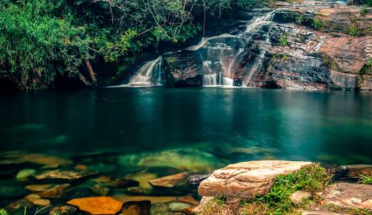 Cachoeira com pedras e água ao fundo Descrição gerada automaticamente com confiança média