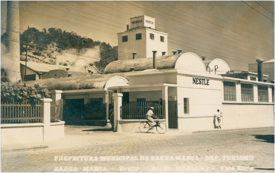 Foto preta e branca de prédio e pessoas na frente de uma casa Descrição gerada automaticamente