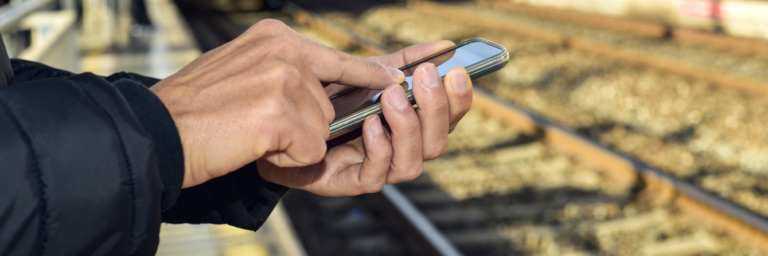 Homem usando smartphone junto à linha ferroviária